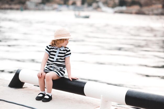 La ragazza divertente del bambino che si siede al molo del mare indossa abiti casual