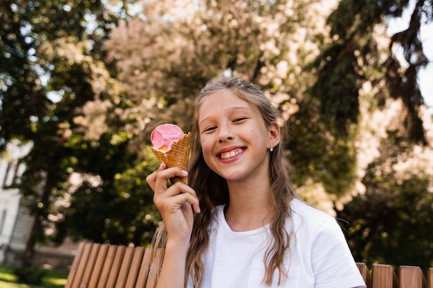 La ragazza divertente del bambino si diverte con il cono gelato nella tazza della cialda Ragazza felice che sorride ridendo e facendo smorfie Pubblicità creativa per gelateria e negozio