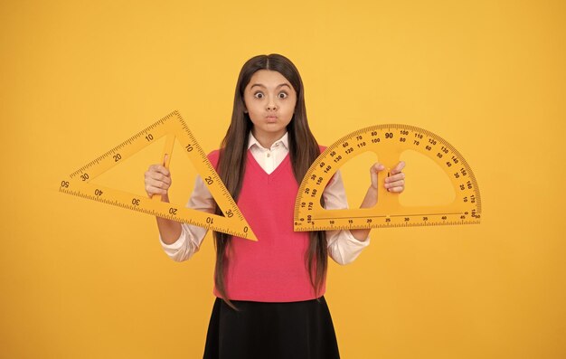 La ragazza divertente del bambino studia la geometria alla lezione scolastica con le discipline del gambo del triangolo e del goniometro