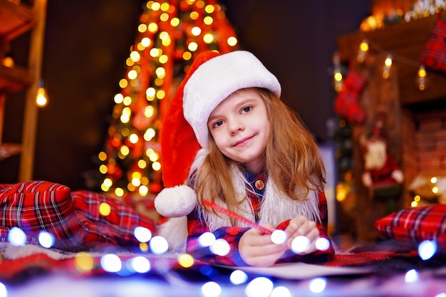 La ragazza divertente in cappello della Santa scrive la lettera a Santa