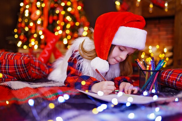 La ragazza divertente in cappello della Santa scrive la lettera a Santa