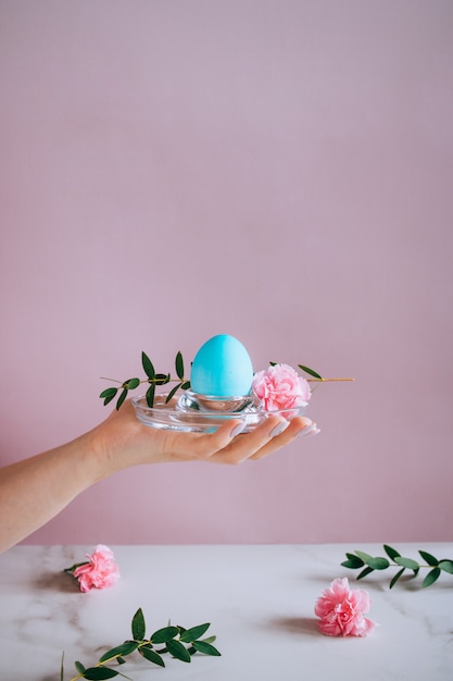 La ragazza è in possesso di un uovo di mangiatore di blu su un basamento, sfondo rosa e marmo, minimalismo, fiori