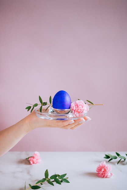 La ragazza è in possesso di un uovo di Pasqua viola su uno sfondo di stand, rosa e marmo, minimalismo, fiori