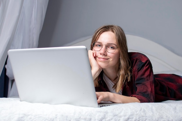 La ragazza è sdraiata a letto con un computer portatile e guarda un video La libera professionista lavora a casa