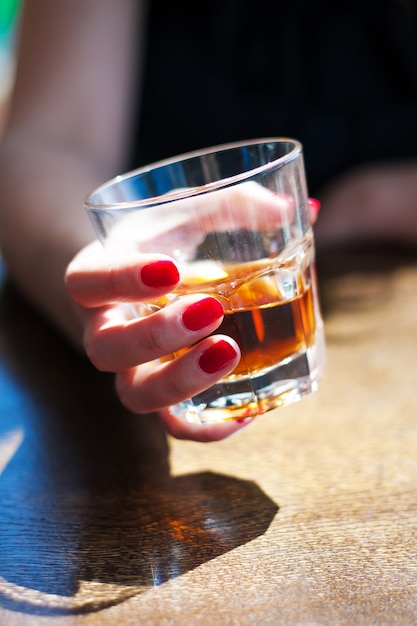 La ragazza è seduta in un bar e tiene in mano un bicchiere di whisky