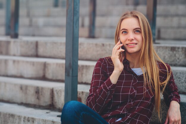 La ragazza è seduta sui gradini e parla al telefono