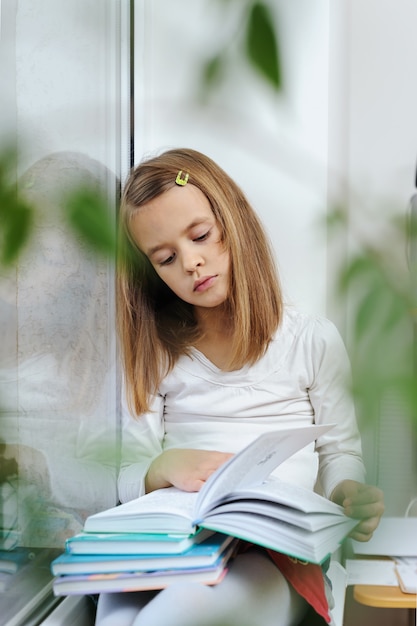 La ragazza è seduta sul davanzale della finestra e legge un libro.