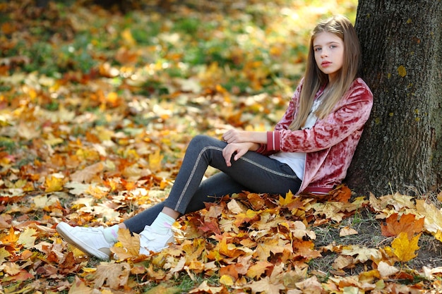 La ragazza è seduta vicino a un grande albero nel parco autunnale