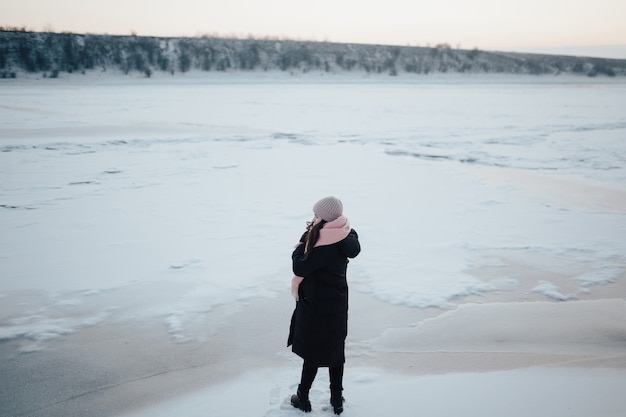 La ragazza è sola vicino al fiume ghiacciato con la schiena e guarda il paesaggio.