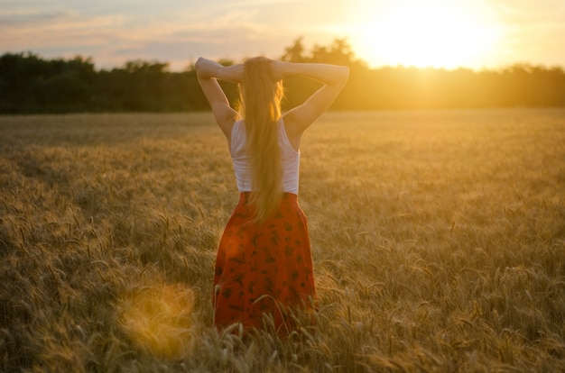 La ragazza è tornata in un campo di grano con le mani dietro la testa