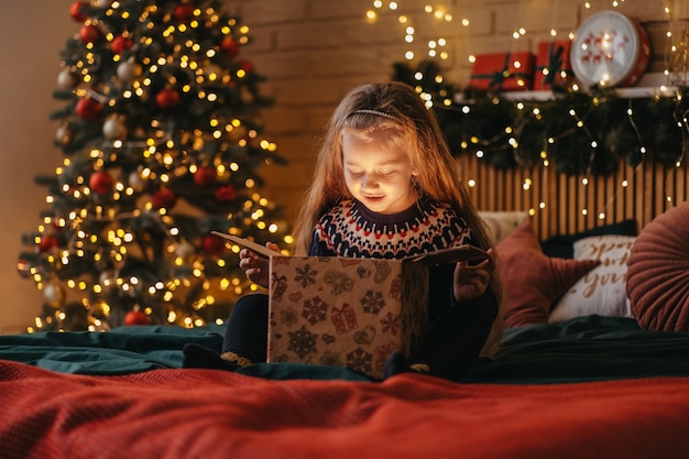 La ragazza eccitata apre la confezione regalo di Babbo Natale, l'infanzia felice, la celebrazione delle vacanze, il miracolo di Natale