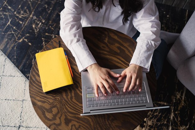 La ragazza europea in una camicia bianca lavora su un computer portatile e sorride