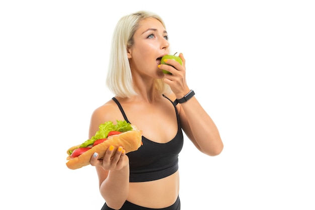 La ragazza europea in uniforme sportiva mostra una mela e un fast food