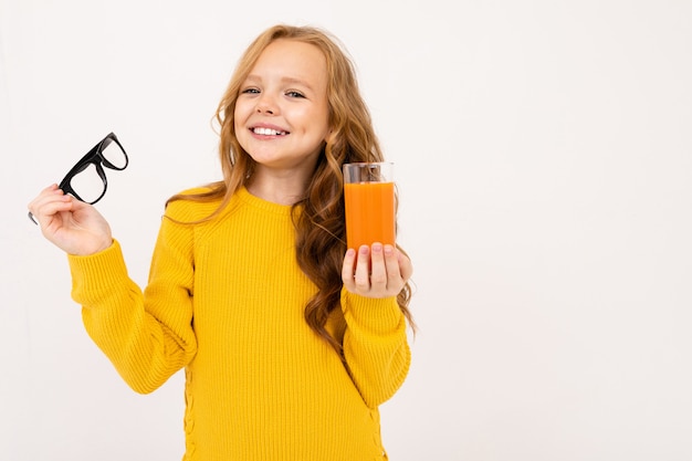 La ragazza europea sorridente si è tolta gli occhiali e tiene in mano un bicchiere di succo di carota