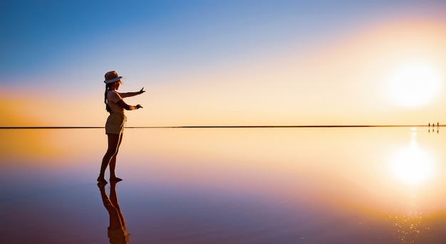 La ragazza felice adorabile cammina e posa in una posa magica lungo il lago salato rosa dello specchio