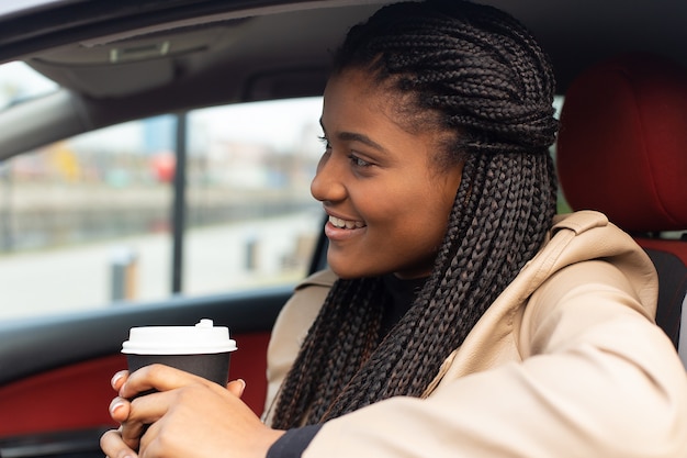 La ragazza felice che guida una macchina che beve caffè, afro-americano