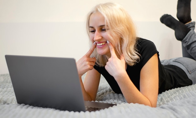 La ragazza felice comunica tramite videochiamata. Sdraiato sul letto a casa. Comunicazione remota. Amore in lontananza.