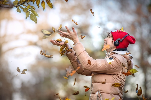 La ragazza felice con il berretto rosso cammina in autunno Park e cattura le foglie che cadono