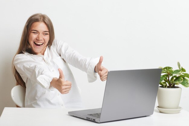 La ragazza felice con il computer portatile si rallegra su sfondo bianco