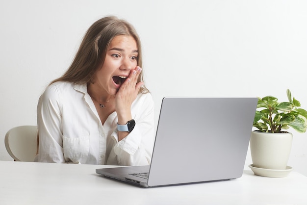 La ragazza felice con il computer portatile si rallegra su sfondo bianco