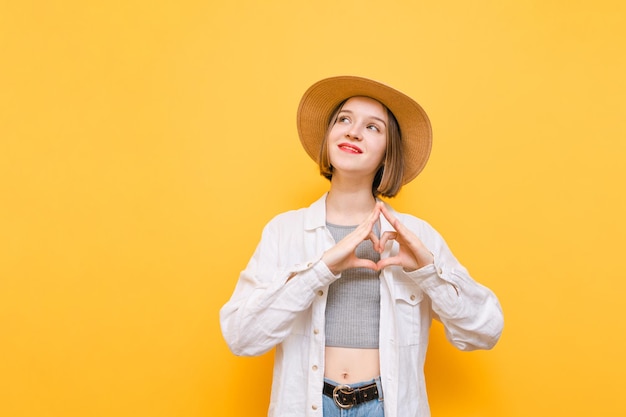 La ragazza felice con un cappello e vestiti in vacanza sta su uno sfondo giallo distoglie lo sguardo