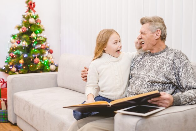 La ragazza felice con un nonno ha letto il libro vicino all'albero di natale