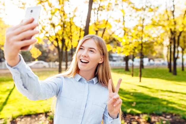 La ragazza felice con un telefono, prende le immagini di se stessa, nel parco, selfie