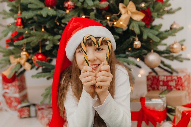 La ragazza felice del bambino sta tenendo i bastoncini di zucchero di Natale. Bambina felice felice alla vigilia di Natale. Bambino pieno di speranze. Vigilia di Capodanno.