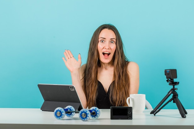 La ragazza felice del blogger sta mostrando ciao gesto davanti alla telecamera su sfondo blu