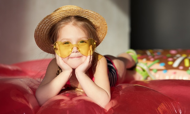 La ragazza felice del piccolo bambino in un costume da bagno e un cappello di paglia prepara per un viaggio dell'estate a casa