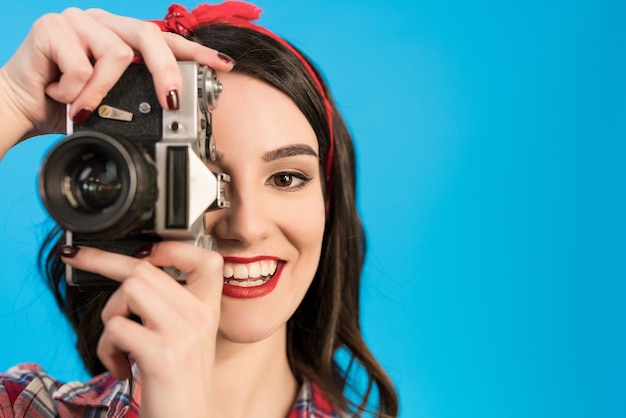 La ragazza felice scatta una foto con una fotocamera retrò sullo sfondo blu