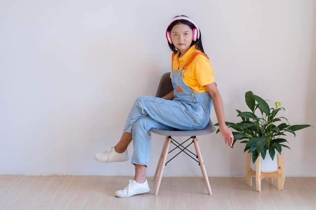 La ragazza felice seduta su una sedia che ascolta la musica in una stanza minima a casa