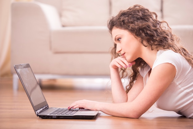 La ragazza felice sta trovandosi sul pavimento e sta lavorando ad un computer portatile.