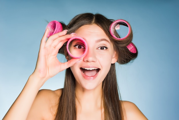 La ragazza felice vuole essere bella, sulla sua testa e nelle sue mani grandi bigodini rosa