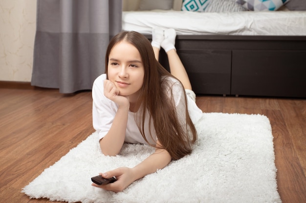 La ragazza giace a casa con un telecomando in mano e guarda la tv