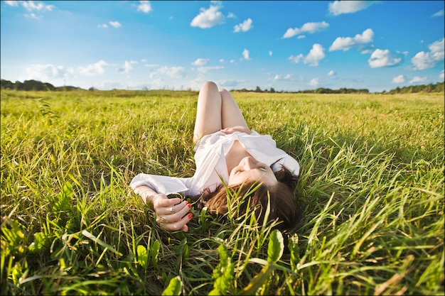 La ragazza giace sull'erba. Bella ragazza sorridente felice che si trova fra erba e fiori. su uno sfondo blu.