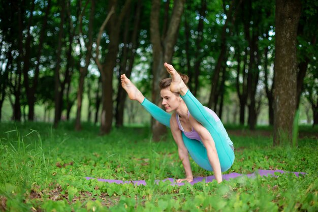 la ragazza giovane di sport pratica lo yoga in una foresta verde chiusa di estate, posizione di assans di yoga. Meditazione e unità con la natura