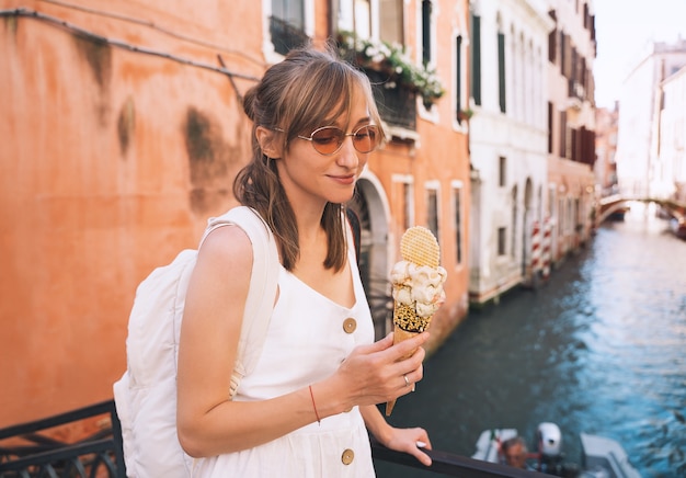 la ragazza gode del bellissimo e delizioso gelato italiano nel cono di cialda sui ponti panoramici di venezia