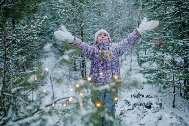 La ragazza gode della prima neve durante la famiglia che cammina nella foresta nel paese delle meraviglie invernale di giorno di nevicata