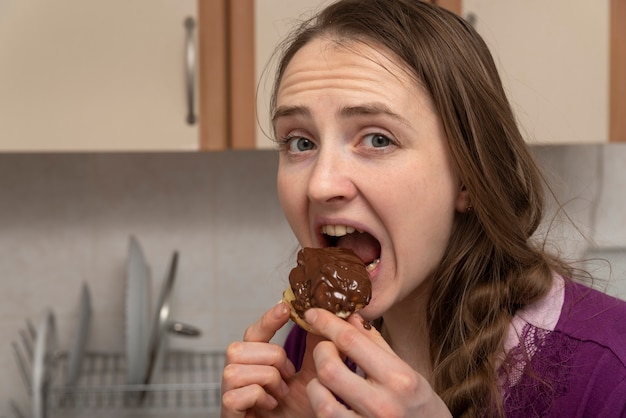 La ragazza golosa mangia l'eclair con la glassa al cioccolato. Dolci proibiti