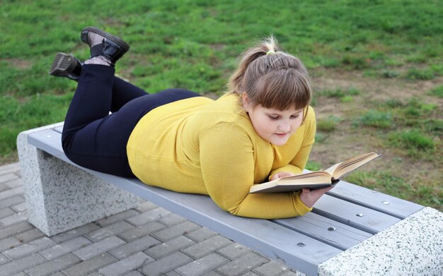 La ragazza grassoccia soddisfatta giace da sola sulla panchina del parco e legge un libro