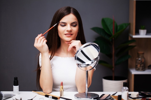 La ragazza graziosa applica il trucco sul fronte a casa vicino allo specchio