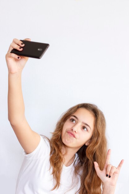 La ragazza graziosa dell&#39;adolescente con capelli lunghi fa il selfie con la faccia di risata divertente