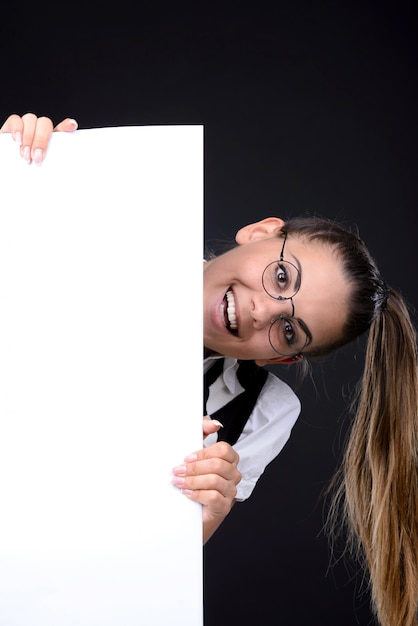 La ragazza guarda fuori da dietro un cartello bianco e sorride.