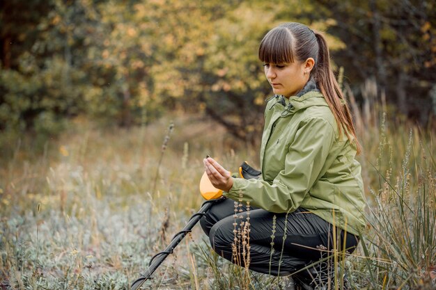 La ragazza guarda il monitor di un metal detector sullo sfondo della foresta