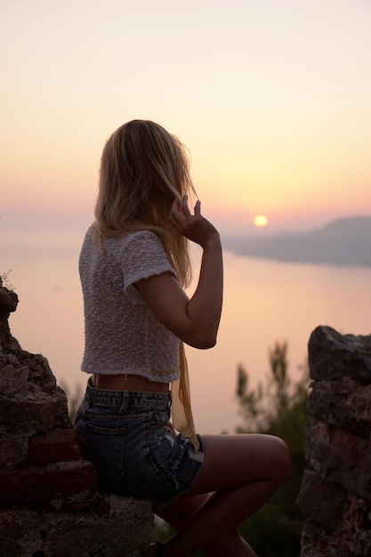 La ragazza guarda il tramonto sul mare da un punto alto. Foto verticale con schiena di donna