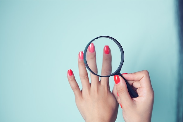 La ragazza guarda le unghie dipinte con una lente d'ingrandimento