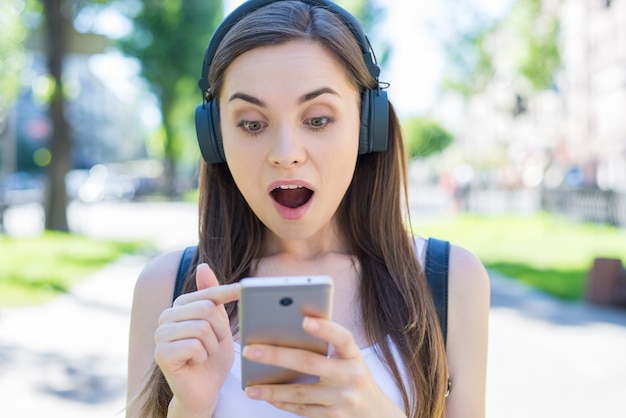 La ragazza ha aperto la bocca scioccata con cuffie e smartphone