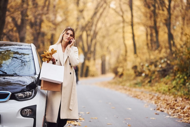 La ragazza ha una chiamata quando si trova vicino alla macchina. Automobile nuova di zecca moderna nella foresta.