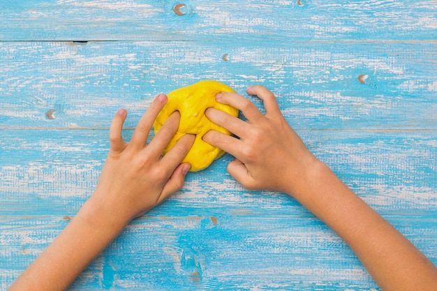 La ragazza impasta una palla di slayma giallo sulla tavola di legno blu.